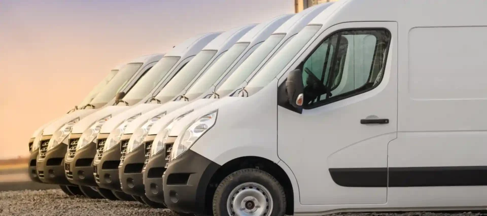 Linha de carrinhas brancas estacionadas em fila, prontas para uso comercial ou logístico.